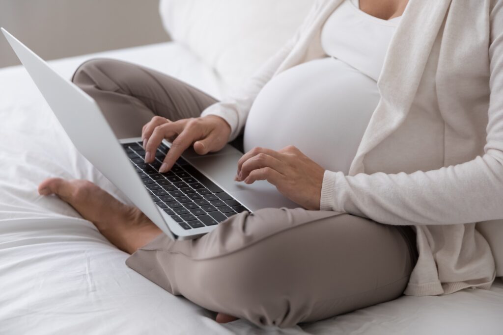 Cropped close up shot of a pregnant woman sitting on bed with laptop