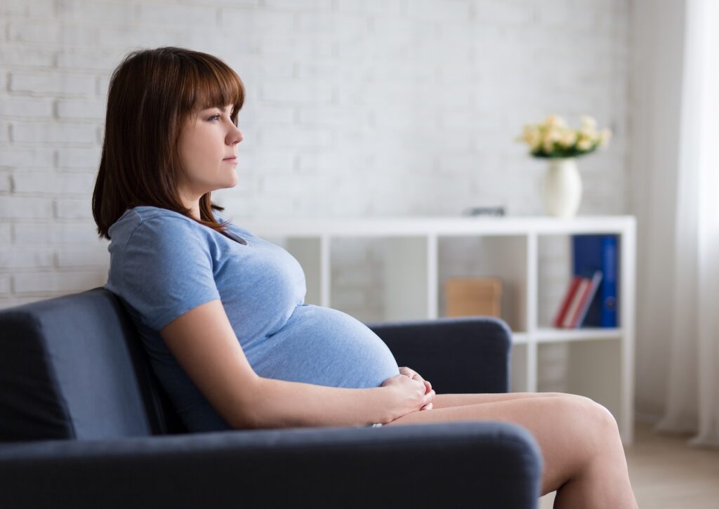 Young pregnant woman sitting on sofa in her living room, looking off thoughtfully