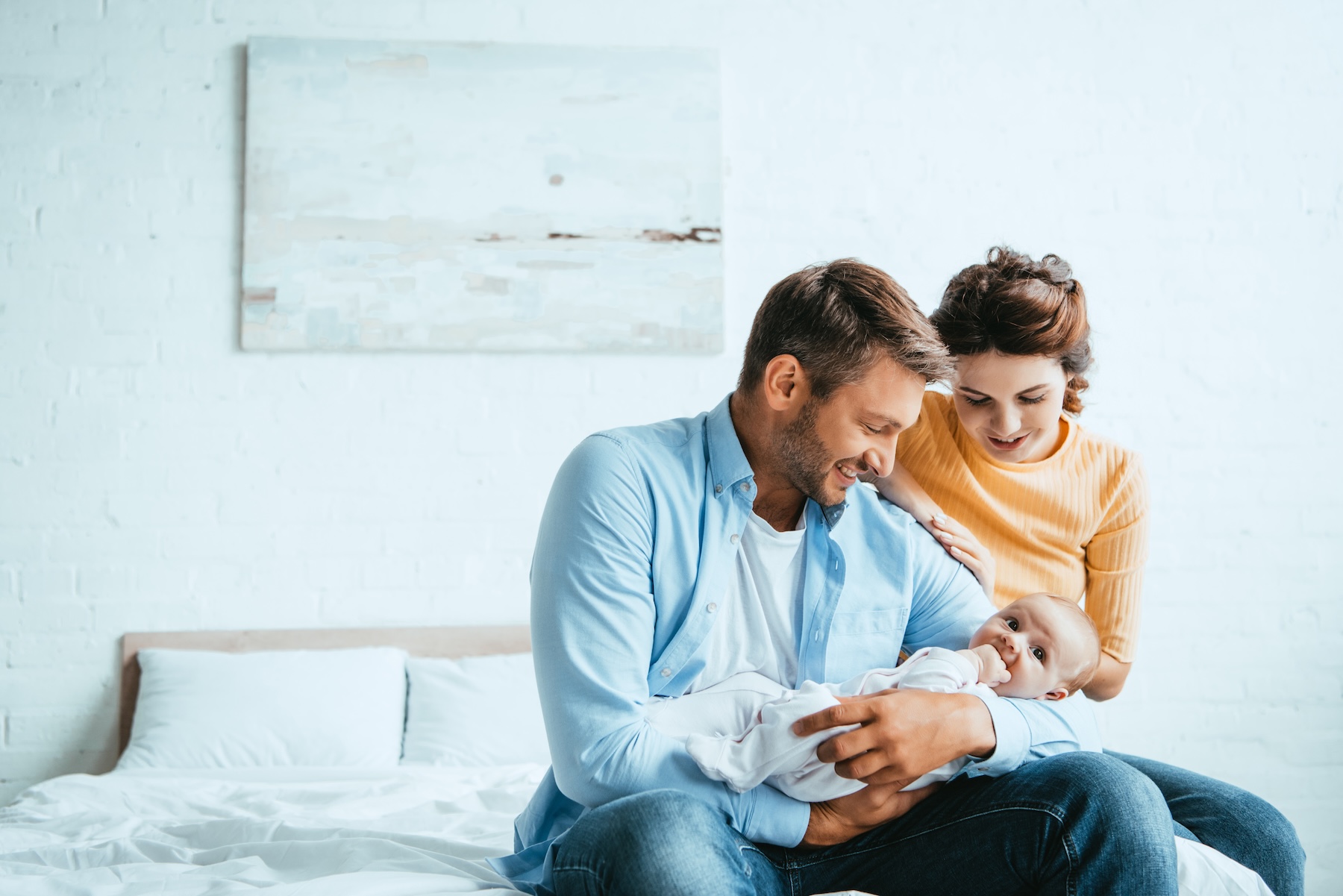Husband and wife holding newborn adopted baby while sitting on bed