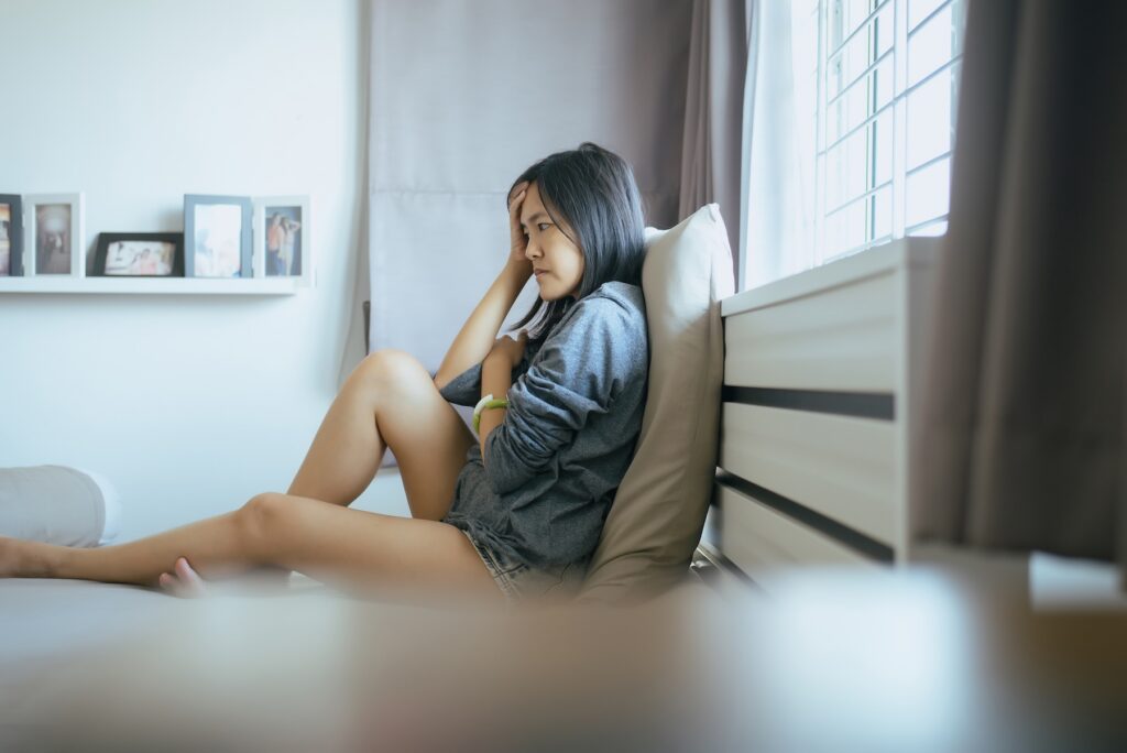 Young women sitting on bedroom at home, feeling worried and confused