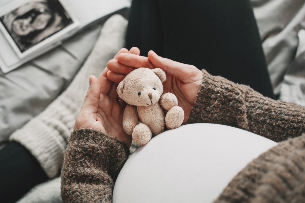 Close up of a woman's pregnant belly with little teddy toy bear.