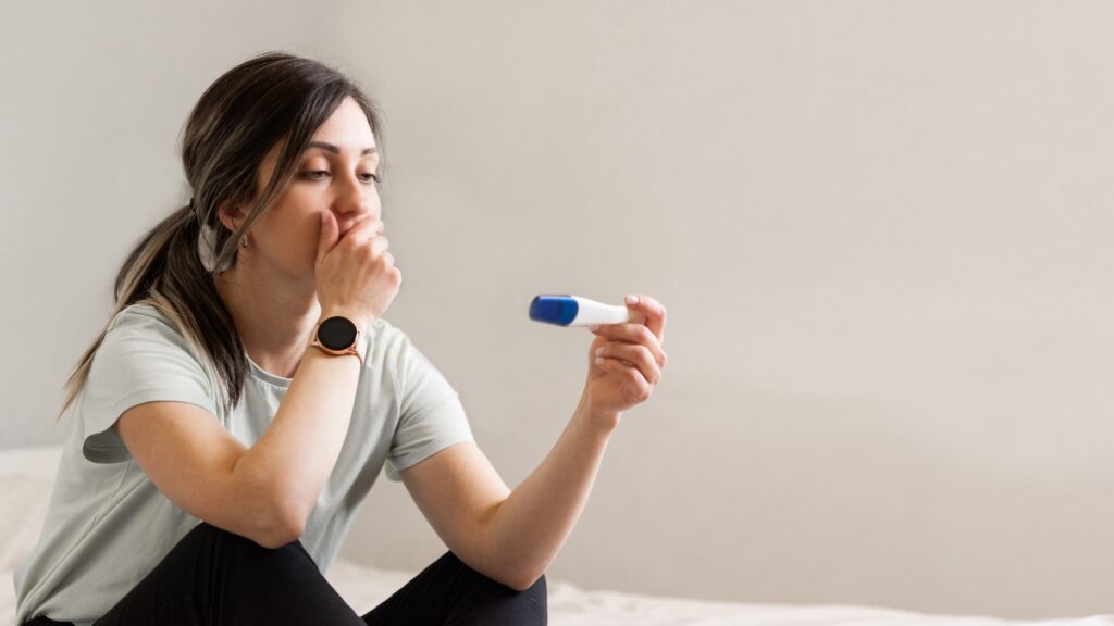 Worried young woman sitting on floor, looking at positive pregnancy test